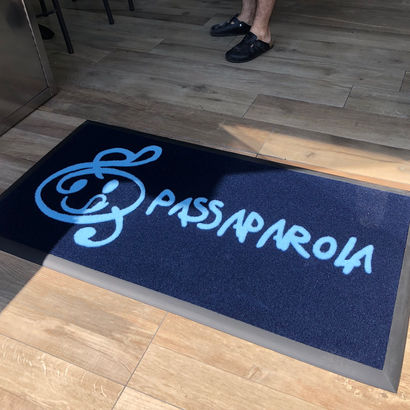Tappeto personalizzato con logo "Passaparola" su fondo nero, realizzato per l'ingresso di un'attività commerciale.