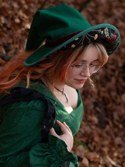 Model mit langem Haar trägt ein grünes Kleid mit floral besticktem Mieder. Passend dazu ein bestickter Hexenhut. Kollektion: Vintage Spell von Silvermoon Threads.