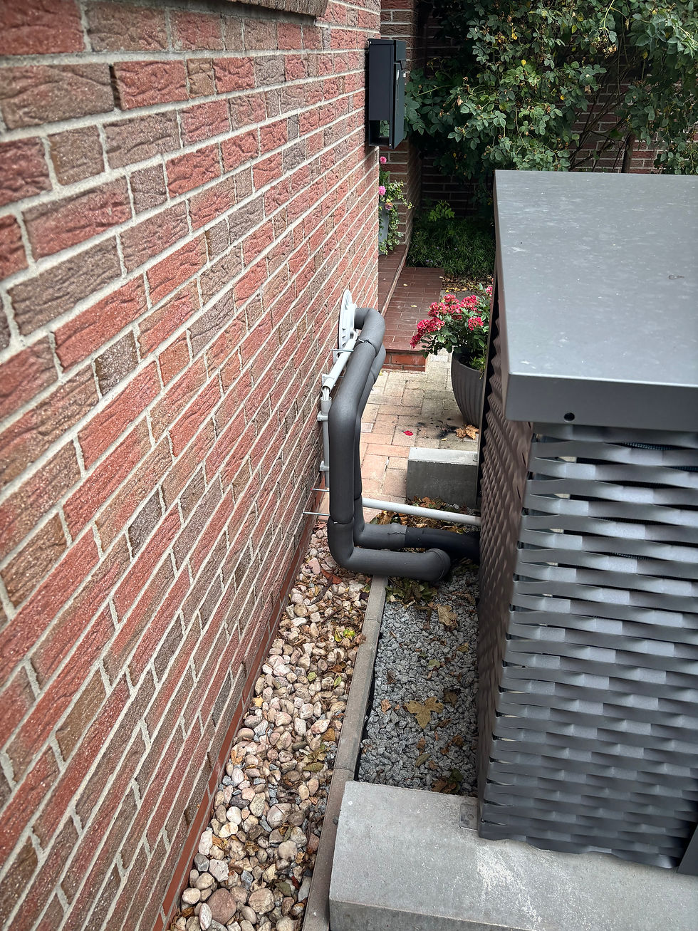 Blick hinter die Außeneinheit der iDM Wärmepumpe: Zu sehen sind die sauber ausgeführten Anschlüsse sowie das stabile Fundament für die Außeneinheit. Die Installation wurde passend zu den örtlichen Gegebenheiten am Reihenendhaus umgesetzt.