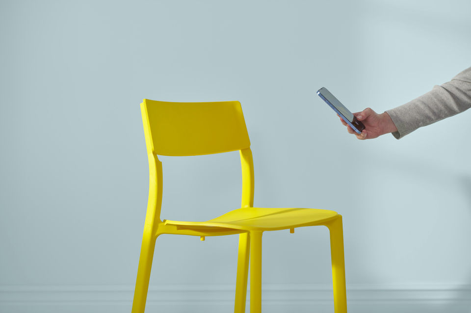 An extended arm reaches into the image. In the hand, holding a phone to take a photo of a yellow chair.