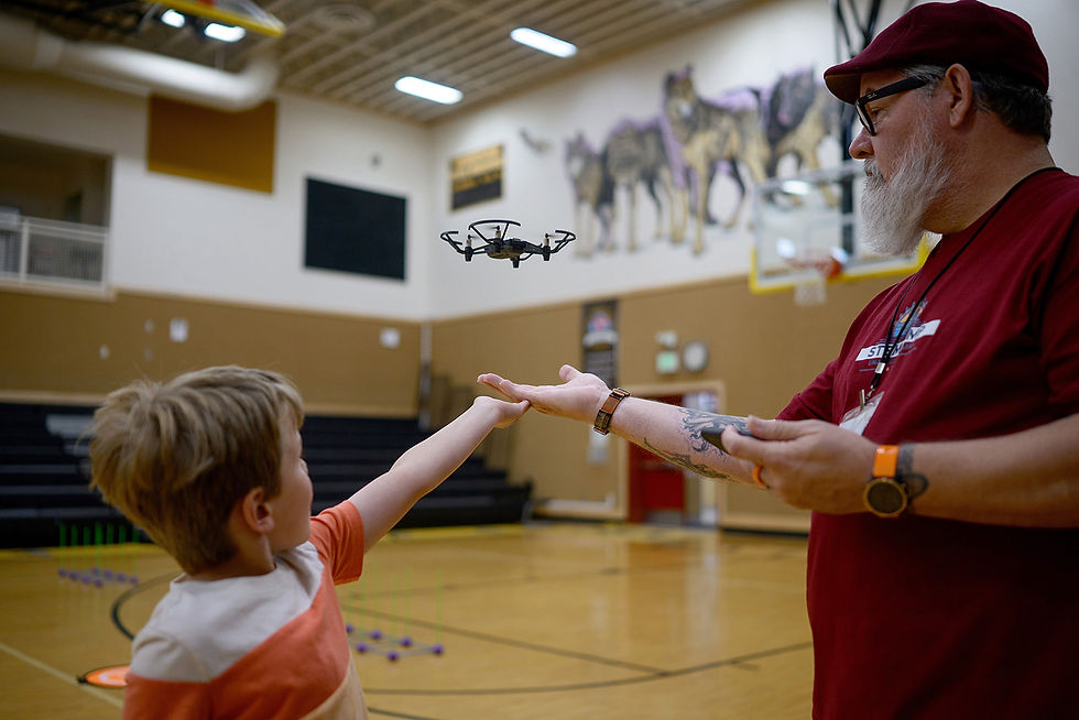Young student and instructor guiding a small indoor educational drone during a STEM activity in a school gymnasium