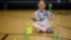 Elementary student flying a mini drone in a school gym as part of a drone curriculum activity with obstacle course challenges for STEM learning.