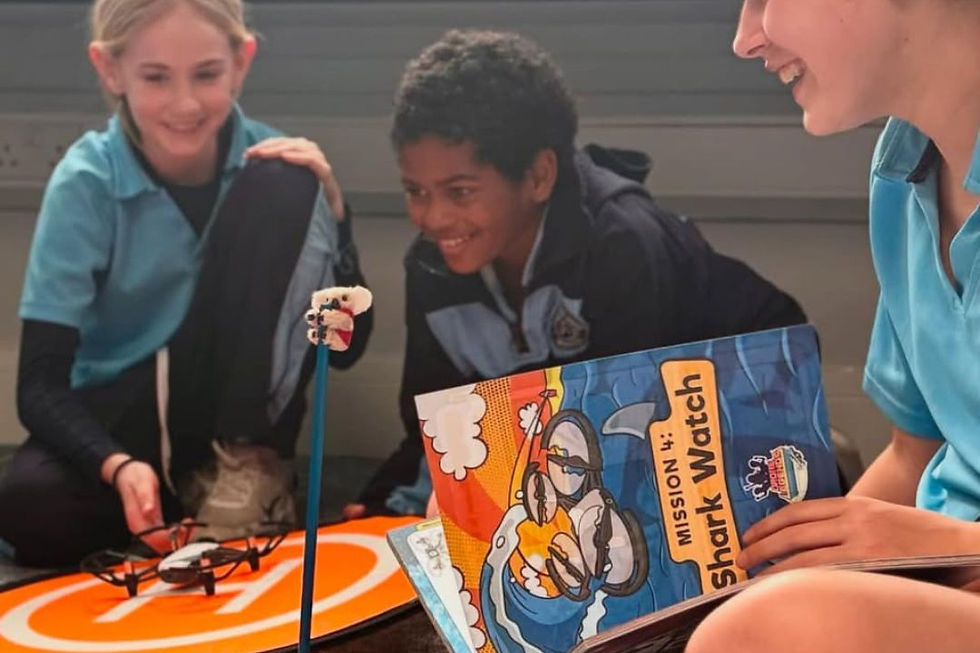 Three upper elementary students engaged in a drone activity, with one student holding a "Mission 4: Shark Watch" guidebook and another launching a drone from a landing pad.