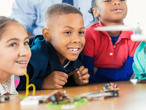 Three fourth grade students watch closely as a small drone hovers during a STEM classroom activity, learning about drone technology, engineering, and problem-solving through hands-on education.