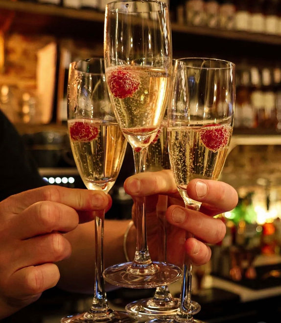 Hands holding three glasses of sparkling wine with raspberries