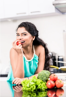 Smiling woman eating tomato, fresh vegetables on counter