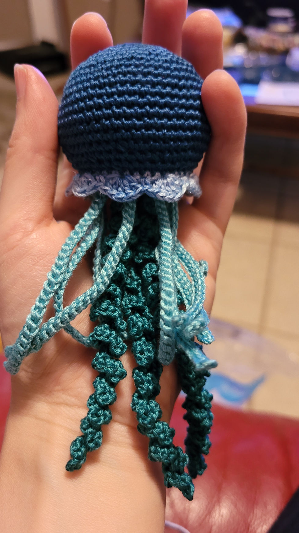A much smaller crocheted jellyfish toy, nestled in the maker's palm.