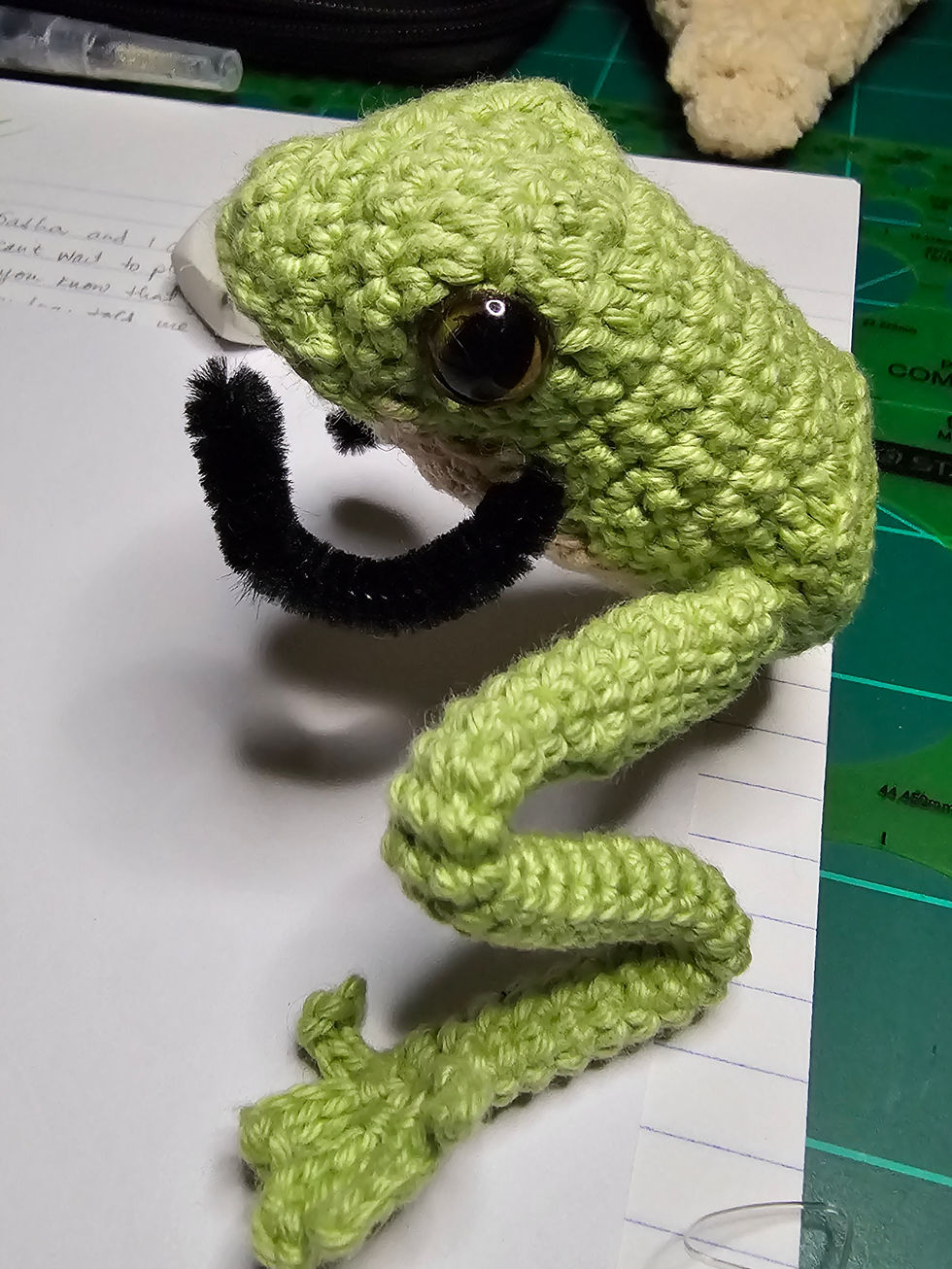 A tiny crocheted frog toy with pipecleaner arms and legs.