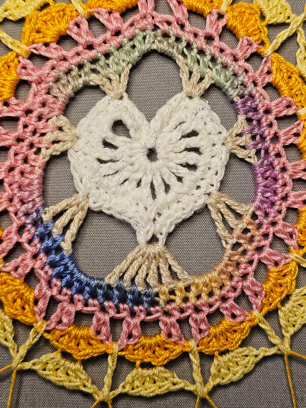 A shining iridescent white heart is suspended in a crocheted dreamcatcher.