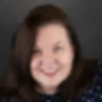 Smiling woman with dark hair in a navy polka-dot top against a gray background.