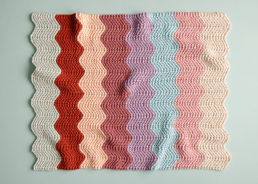 A knit blanket consisting of vertical chevrons in various colours. The blanket has a retro feel.
