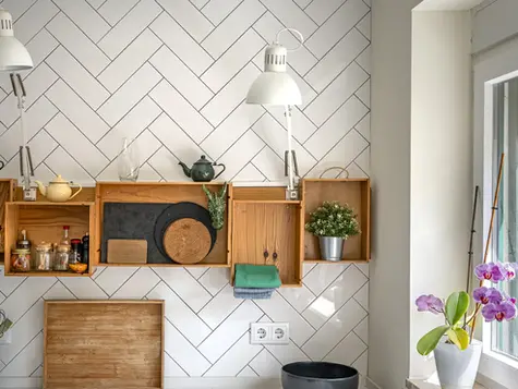 Wooden crate shelves with teapots and a plant on a white tiled kitchen wall
