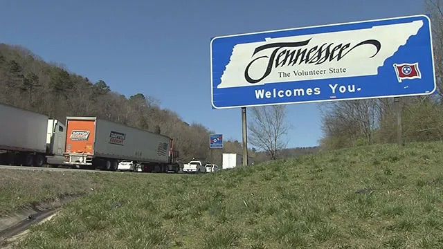 Welcome to Tennessee highway sign along the roadside with trucks traveling in the background under a clear blue sky.