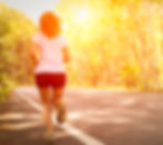A woman jogging down a road at sunrise.