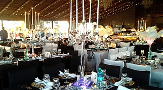 Wedding reception tables arranged beneath a wooden roof with warm hanging lights
