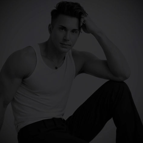 Waymon Hudson in a fitted white tank top and black pants, seated with one knee up and leaning casually forward, exuding confidence and intimacy — promotional photo for Through My Skin album.