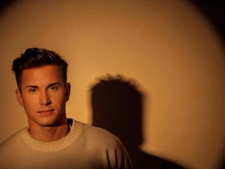 Waymon Hudson, queer writer and musical creator, spotlighted against a warm-toned background with dramatic shadow — representing visibility, storytelling, and creative duality.