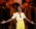 Cynthia Erivo performing “I’m Here” as Celie in The Color Purple on Broadway, standing center stage in bright yellow trousers and singing with arms outstretched, surrounded by the ensemble in warm light.