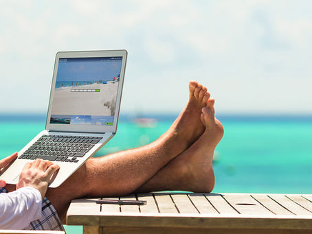Person using a laptop on a wooden table near turquoise ocean water in Costa Rica, symbolizing digital nomad and work-from-paradise lifestyle.