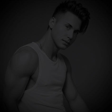 Waymon Hudson in a white tank top against a dark backdrop, gazing directly at the camera with a soft, magnetic expression — sensual portrait for the Through My Skin album.