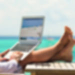 Person using a laptop on a wooden table near turquoise ocean water in Costa Rica, symbolizing digital nomad and work-from-paradise lifestyle.