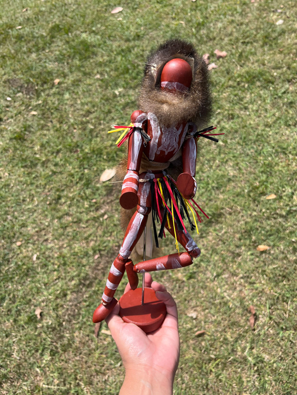 Hand holding a unique manikin in red and white clothing on green grass.
