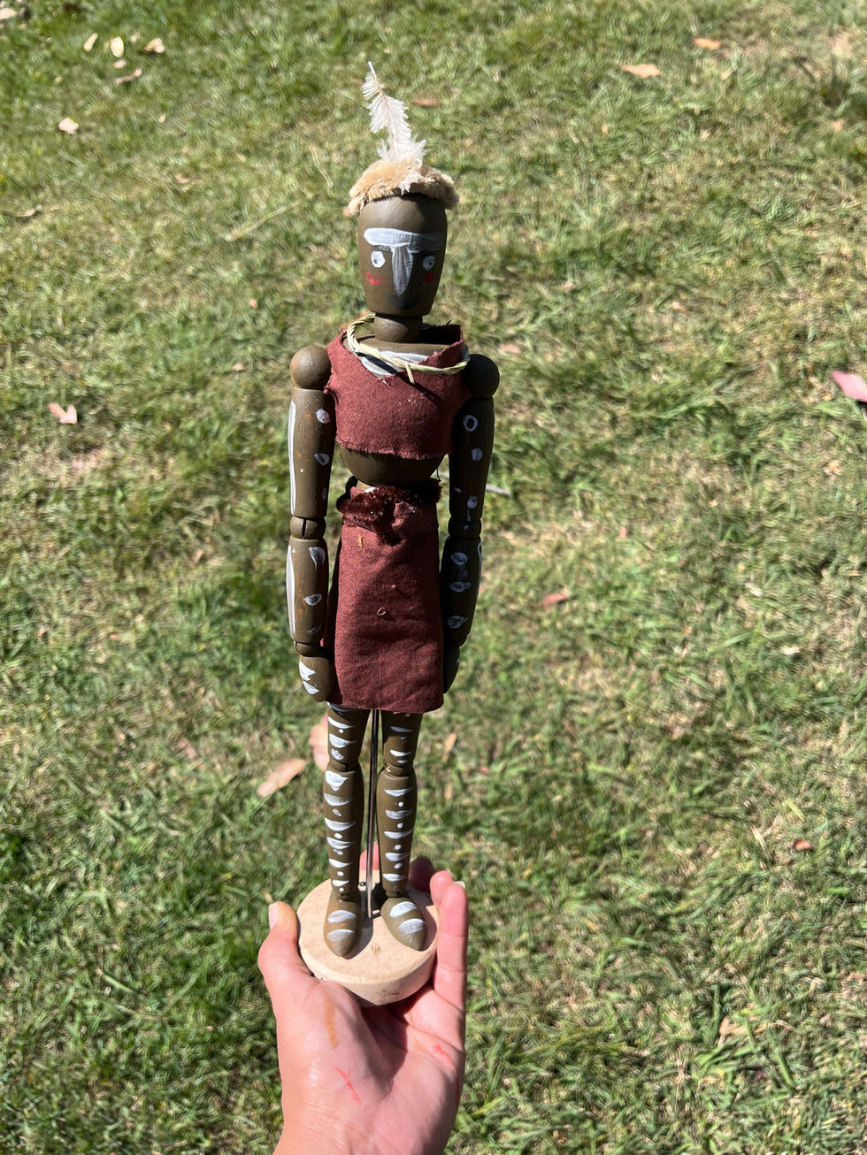 Hand holding a wooden doll with details and textures on the grass background.