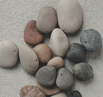 A collection of smooth river stones in varied shades of gray, beige, white, terracotta, and charcoal, evoking the weight and complexity of living with binge eating disorder