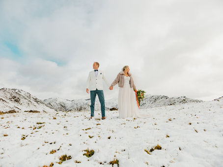 Couple dressed in their wedding outfits standing on a snow covered mountain during their snow adventure photoshoot