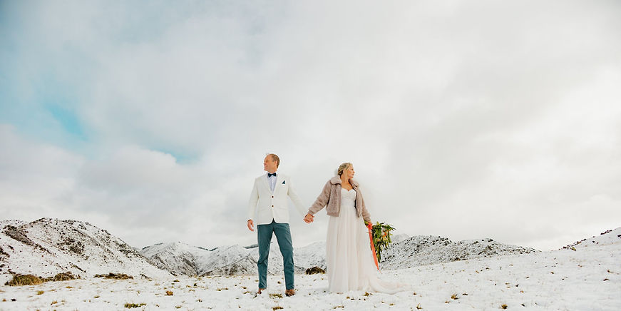 A couple on their elopement day in New Zealand holding hands and standing in the snow on top of Mt. Paradise