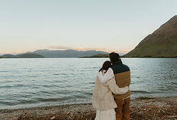 a couple standing side by side holding each other and looking out over Lake Wanaka on their elopement day during sunset Eloping in New Zealand _ Chaznel Photography