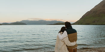 a couple standing side by side holding each other and looking out over Lake Wanaka on their elopement day during sunset Eloping in New Zealand _ Chaznel Photography