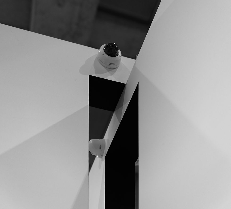 Two dome security cameras mounted on angular white panels in a stark black-and-white interior, with sharp geometric shadows.