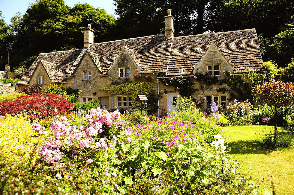 Eye-level view of a honey-coloured stone cottage surrounded by lush greenery
