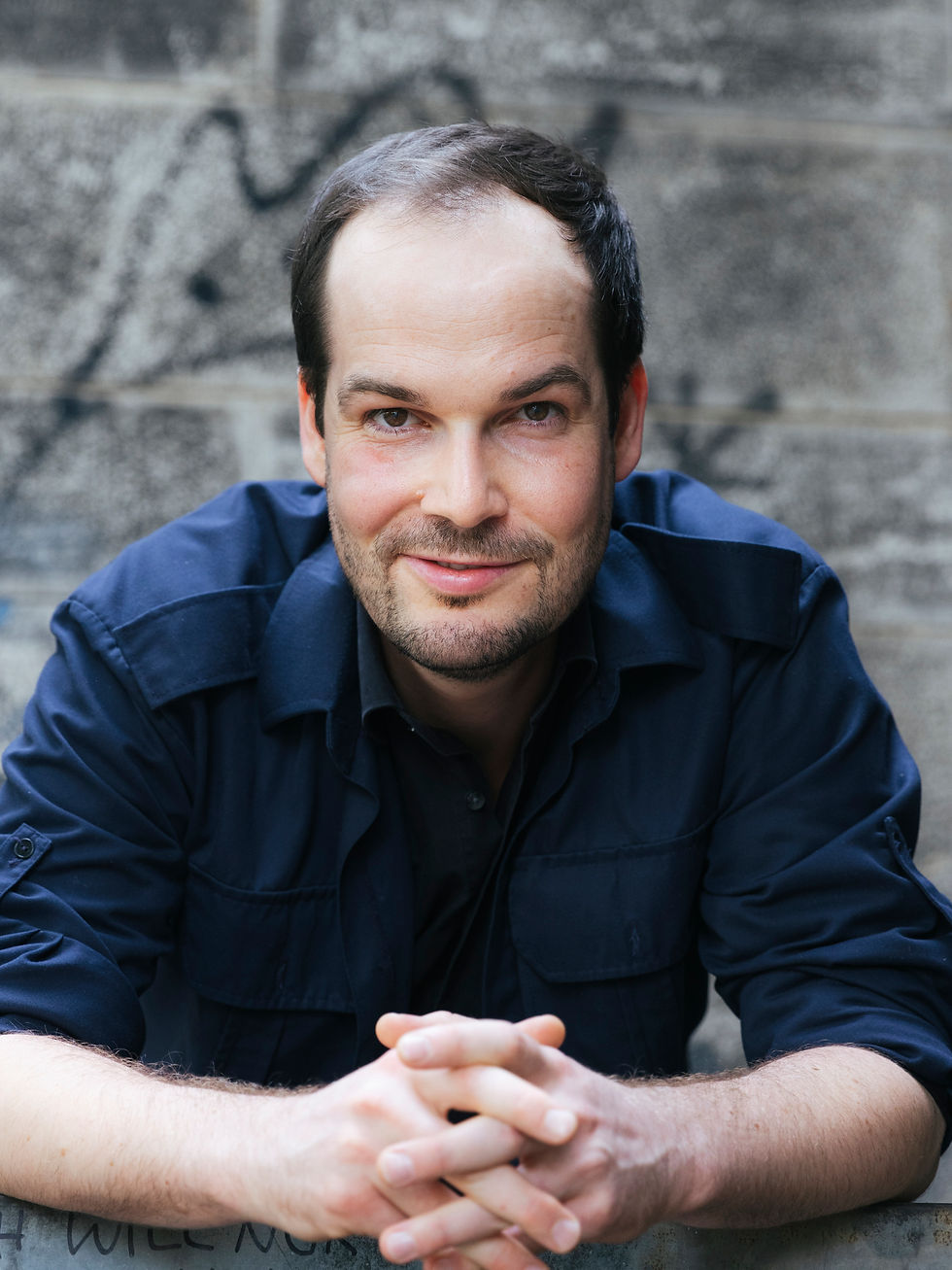 Autor Max Czollek, sitzend, die Hände gefaltet