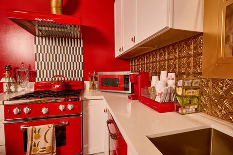 Luxury pinup-inspired French kitchen set in Los Angeles photo studio featuring red and gold interiors, Big Chill retro appliances, black and white checkered floors, burlesque wallpaper, Old Hollywood vanity lights, and a 1950s-style red and gold dining area.