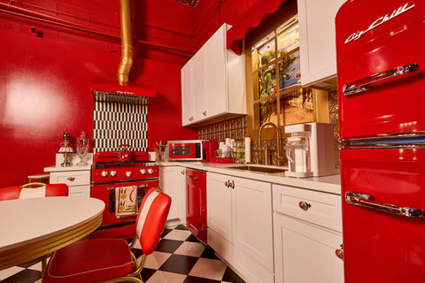 Luxury pinup-inspired French kitchen set in Los Angeles photo studio featuring red and gold interiors, Big Chill retro appliances, black and white checkered floors, burlesque wallpaper, Old Hollywood vanity lights, and a 1950s-style red and gold dining area.