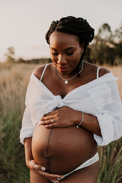 Pregnant mother standing in field wearing a white shirt