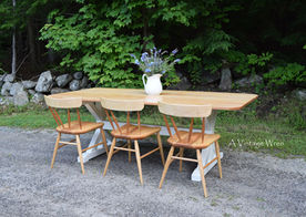 New Hampshire made solid wood trestle dining table and chairs. The table top is a light brown made out of Natural Birch and the trestle base in painted white. The modern chairs are the same light color as the table top.