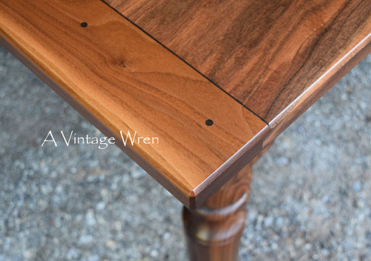 a close up picture of a New Hampshire made farmhouse dining table with breadboard ends. The table top is rich medium to dark brown colored wood made from solid Black Walnut.