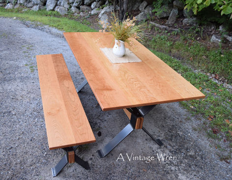 Massachusetts modern industrial trestle dining table and bench set, features a dark metal X style legs with a warm wood top.