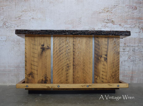 A New Hampshire made home bar in the modern industrial style. The bar top is a live edge slab with an epoxy finish.
The front of the bar is rough cut lumber with gray metal accent strips.
The bar has a wood foot rest with industrial bolts holding it on.