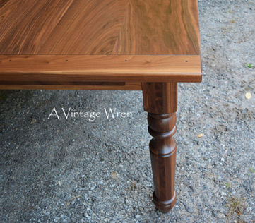 a close up picture of a New Hampshire made farmhouse dining table with breadboard ends. The table top is rich medium to dark brown colored wood made from solid Black Walnut.