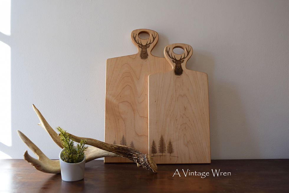 hardwood cutting or charcuterie board with an engraved deer head with antlers on the top and 3 evergreen trees on the bottom.