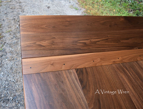 a close up photo of New Hampshire made extendable farmhouse dining table for 8 to 10. The table top is rich medium to dark brown colored wood made from solid Black Walnut, it shows the company board extensions in place
