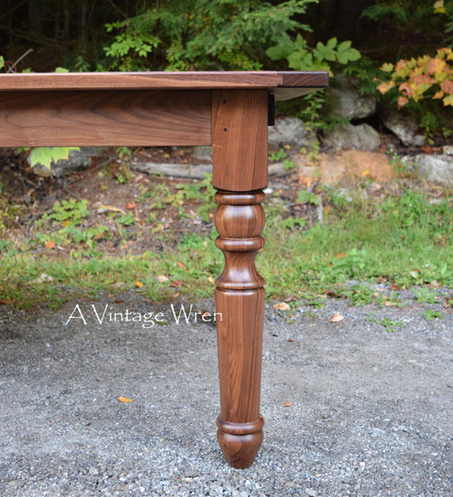 a close up photo of a New Hampshire made farmhouse style dining table leg. The leg is rich medium to dark brown colored wood made from solid Black Walnut.
The legs are turned on a lathe, they are chunky and large in size.