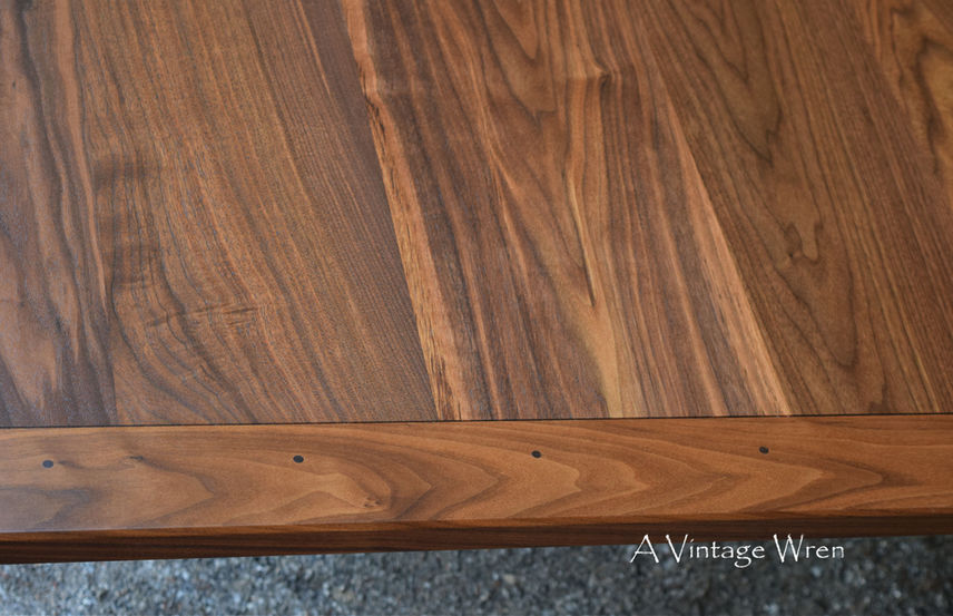 a close up picture of a New Hampshire made farmhouse dining table with breadboard ends. The table top is rich medium to dark brown colored wood made from solid Black Walnut.