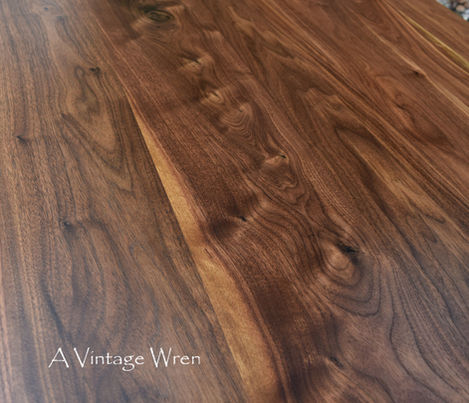 a close up of the grain of walnut table top, it shows the wavy or curly grain and varying colors of light creamy brown to a rich chocolate brown