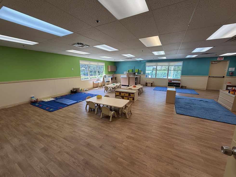 Bright preschool classroom at Explorations in Oviedo with green and teal walls, small tables, and blue rugs