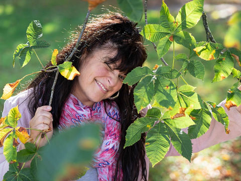 klassisches Portrait Fotografie eine Frau schaut zwischen Kastanienästen mit einem Augenzwinkern in die Kamera